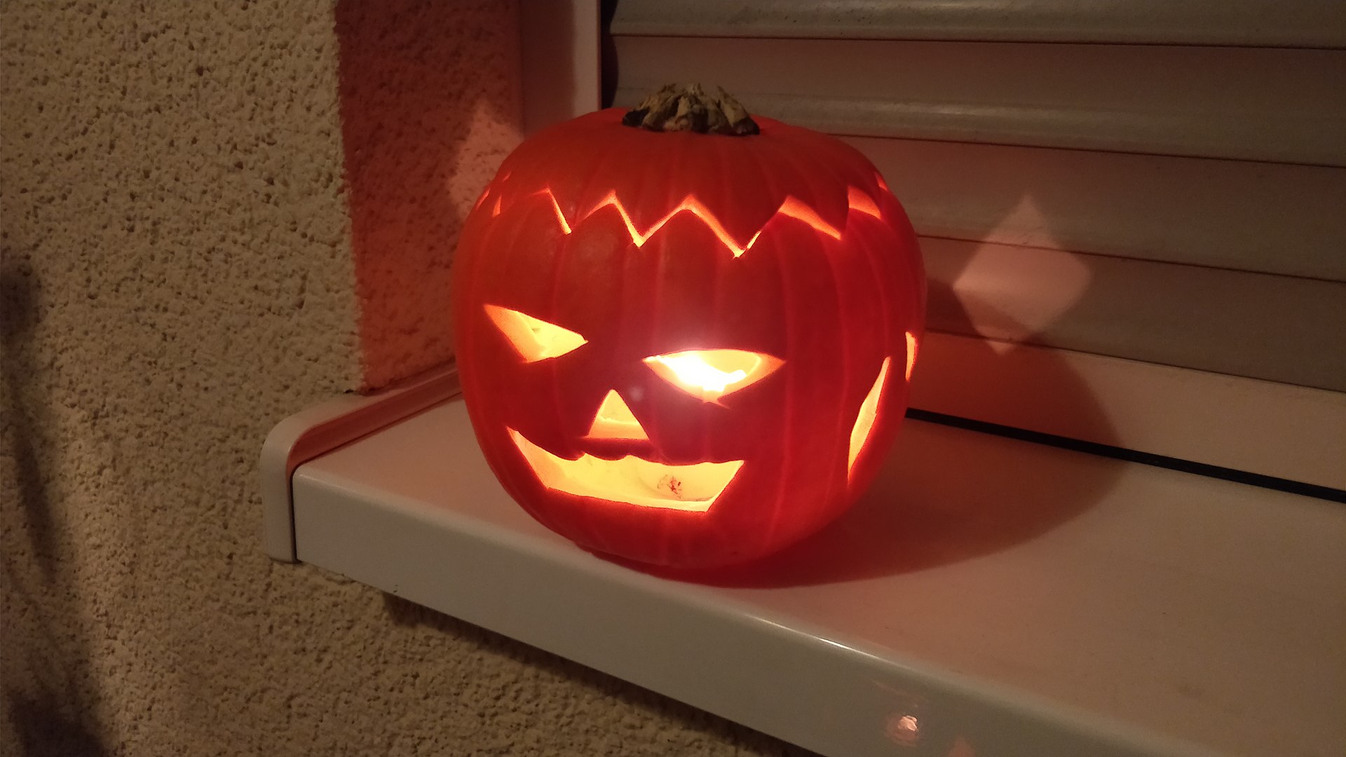 Đèn bí ngô jack-o-lantern khoét mặt cười đặt trên bậu cửa sổ, nến sáng bên trong