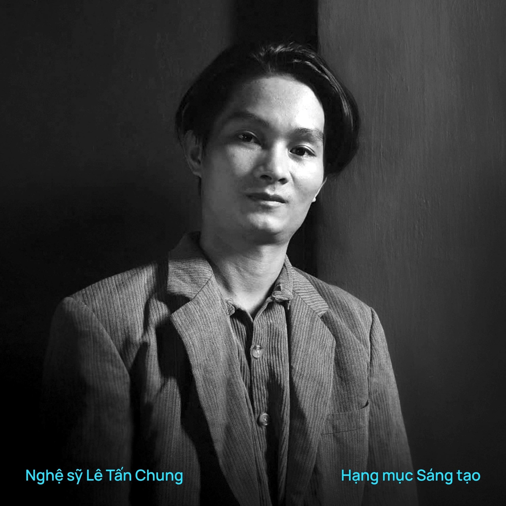 Chân dung đen trắng Lê Tấn Chung, mặc áo khoác vải bố, đứng trước mảng tường tối