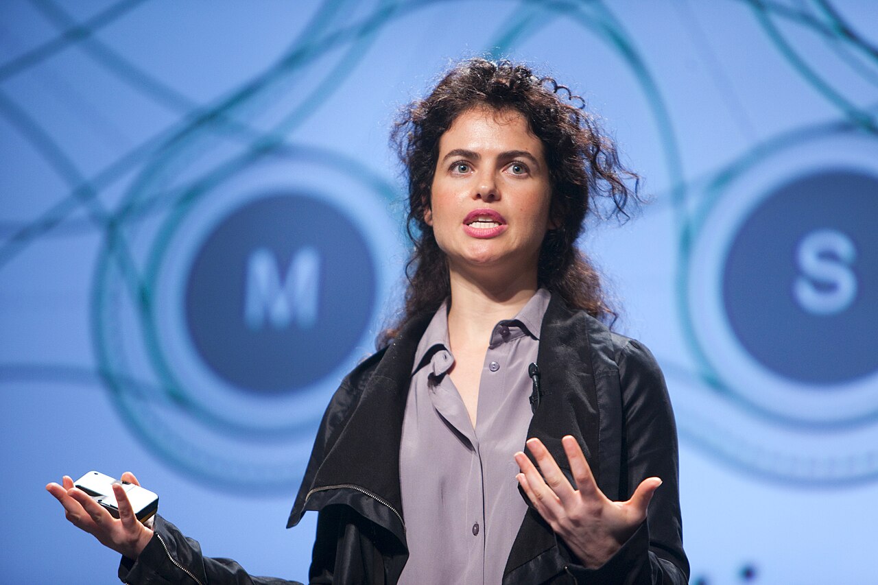 Neri Oxman thuyết trình trên sân khấu với đồ họa mạng lưới sinh học phía sau