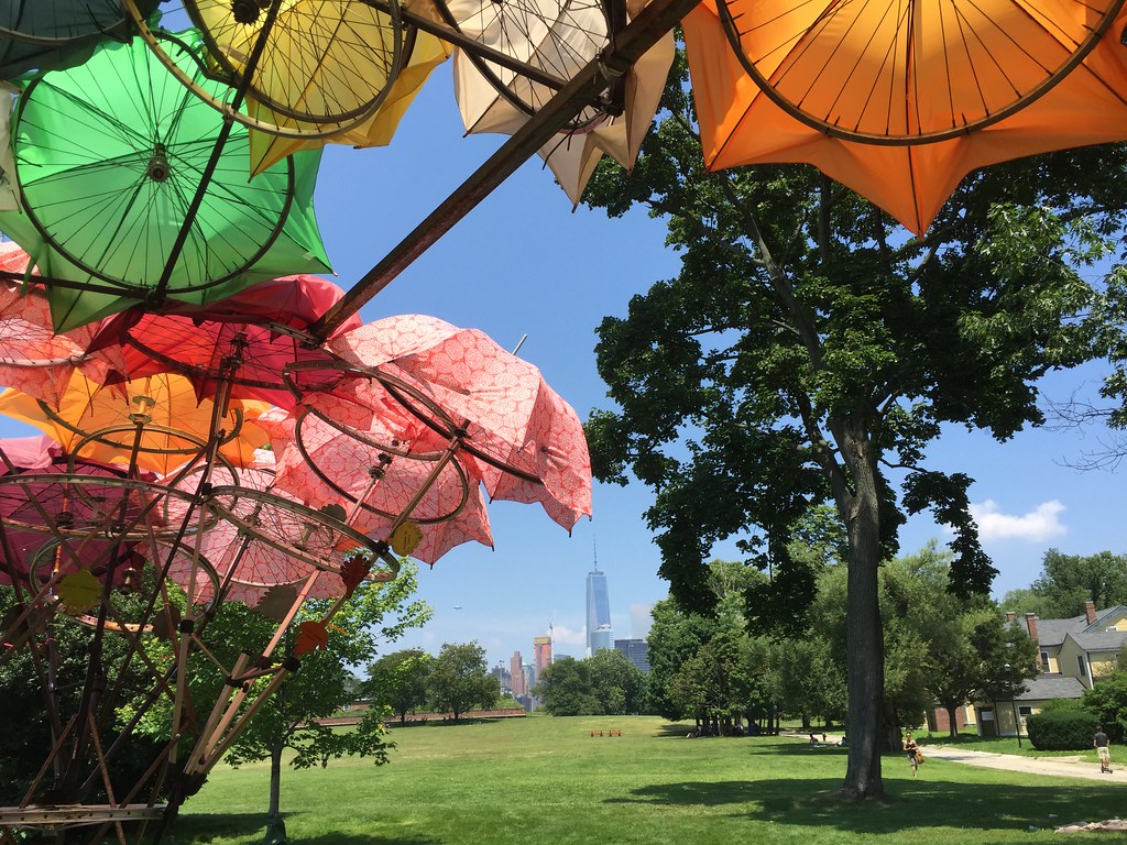 Tán ô xanh lá và cam của Organic Growth Pavilion, phía xa là tháp One World Trade Center nhìn từ Governors Island
