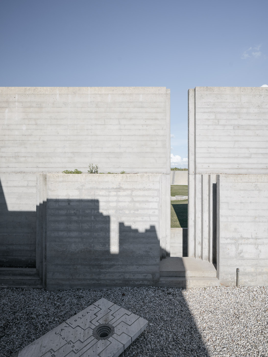 Các mảng tường bê tông xếp lớp của khu mộ Brion do Carlo Scarpa thiết kế, bia khắc tên Scarpa dưới nền sỏi