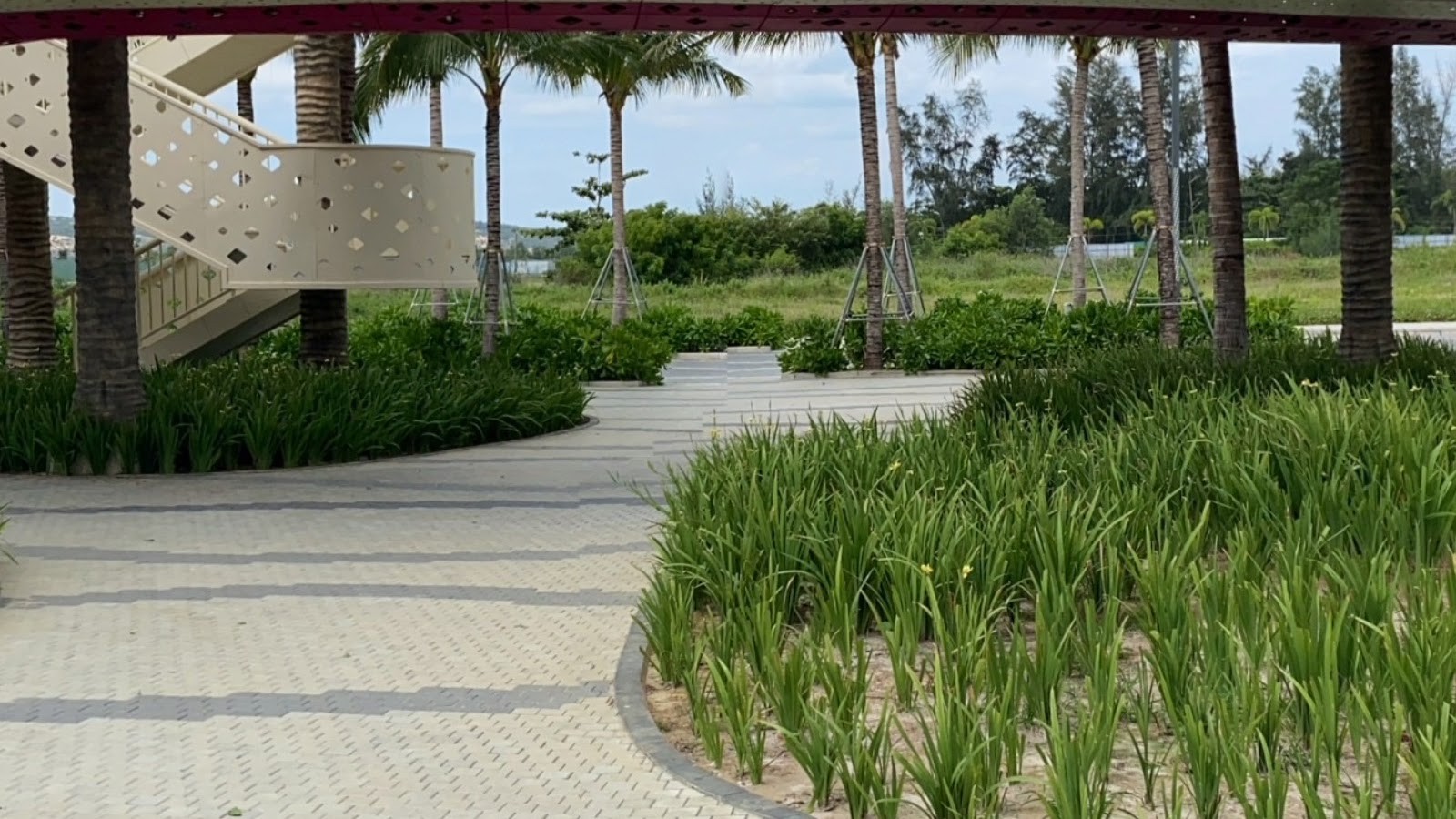 Khối thang lên tuyến cầu bằng bê tông sáng màu đục lỗ tròn, phía trước là luống cỏ trang trí cao ngang thắt lưng