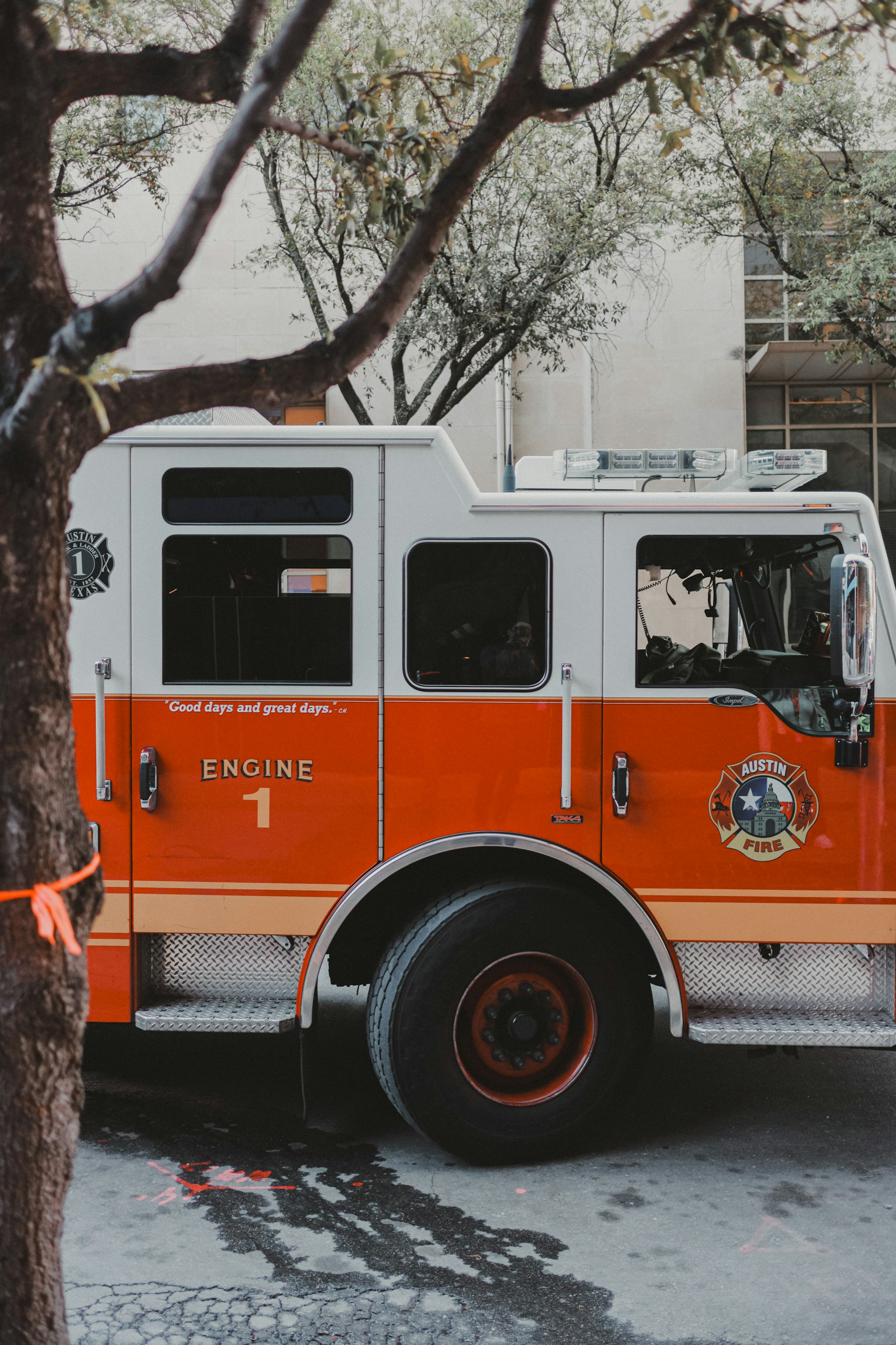 Xe chữa cháy cỡ lớn màu cam trắng đỗ dưới tán cây, trên thân xe có chữ AUSTIN FIRE và ENGINE 1