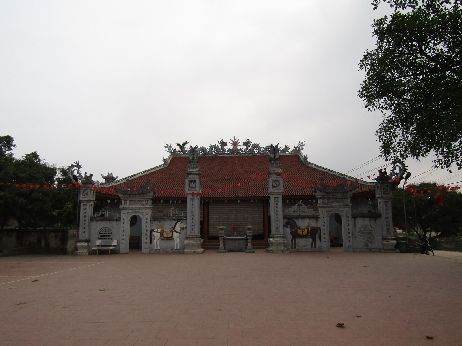 Một ngôi đình làng nhìn thẳng từ sân, mái ngói hai tầng, cột gỗ đỡ hiên, trời nhiều mây