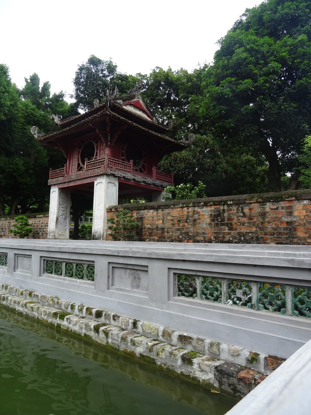 Gác gỗ sơn đỏ hai tầng đứng cạnh hồ nước nhỏ, tường gạch bao quanh có cửa tròn