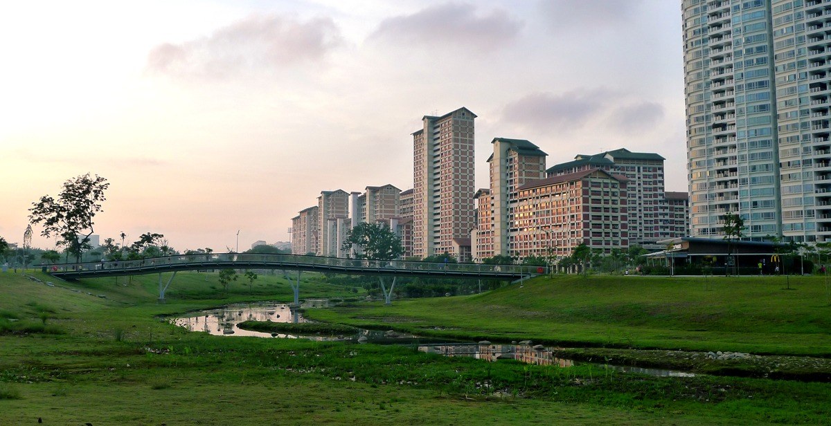 Bishan–Ang Mo Kio Park, Singapore — cầu đi bộ bắc qua dòng suối nhỏ lúc hoàng hôn, bãi cỏ và nhà cao tầng khu dân cư phía sau