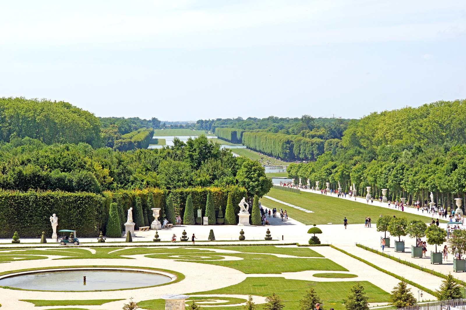 Nhìn từ sân thượng xuống trục vườn Versailles: bãi cỏ dài viền hàng cây cắt xén thẳng tắp hai bên, xa xa là một đoạn kênh nước giữa rừng.