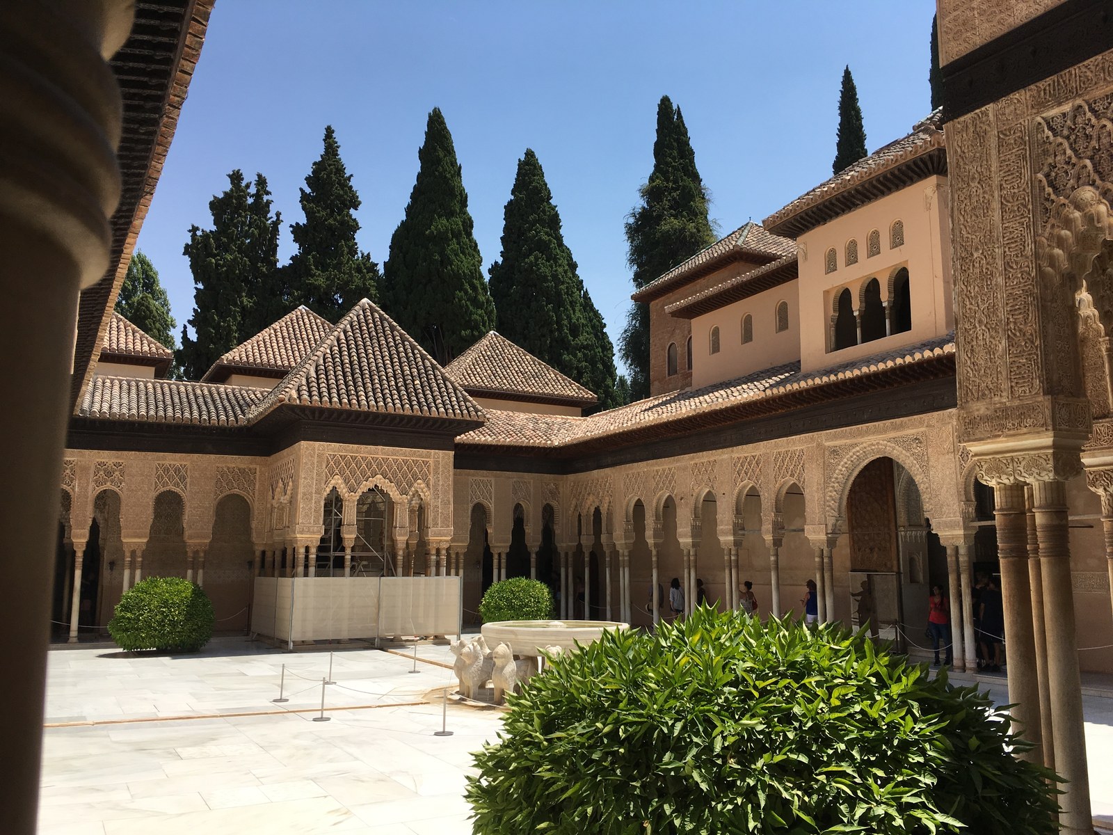 Sân trong Court of the Lions tại cung điện Alhambra, mái ngói nâu chạm khắc tinh xảo, các mái vòm nhọn kiểu Hồi giáo, hàng cây bách phía sau