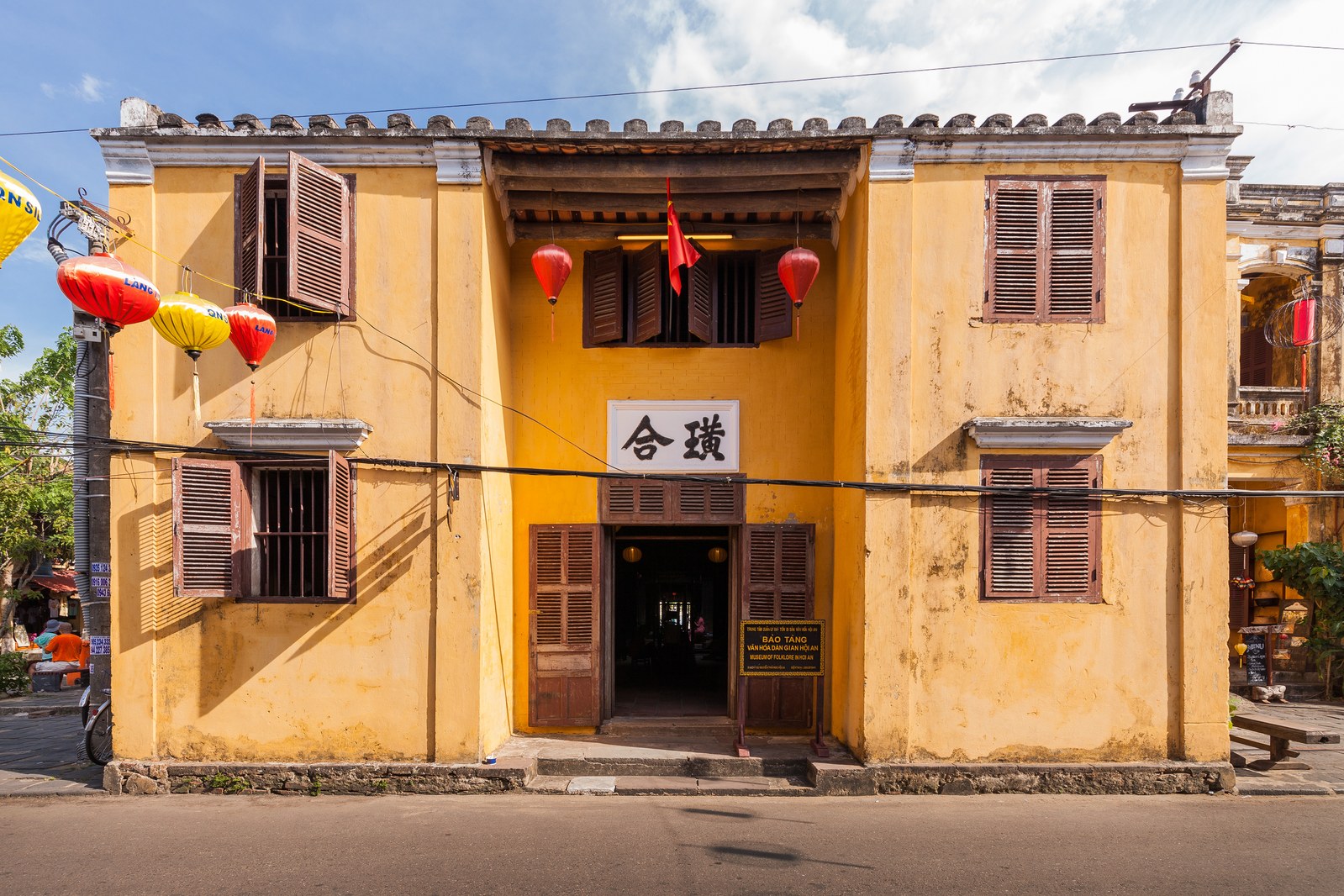Ngôi nhà cổ hai tầng màu vàng ở Hội An với cửa chớp gỗ nâu, đèn lồng đỏ vàng treo trước cửa, biển đề Bảo tàng Văn hóa Dân gian