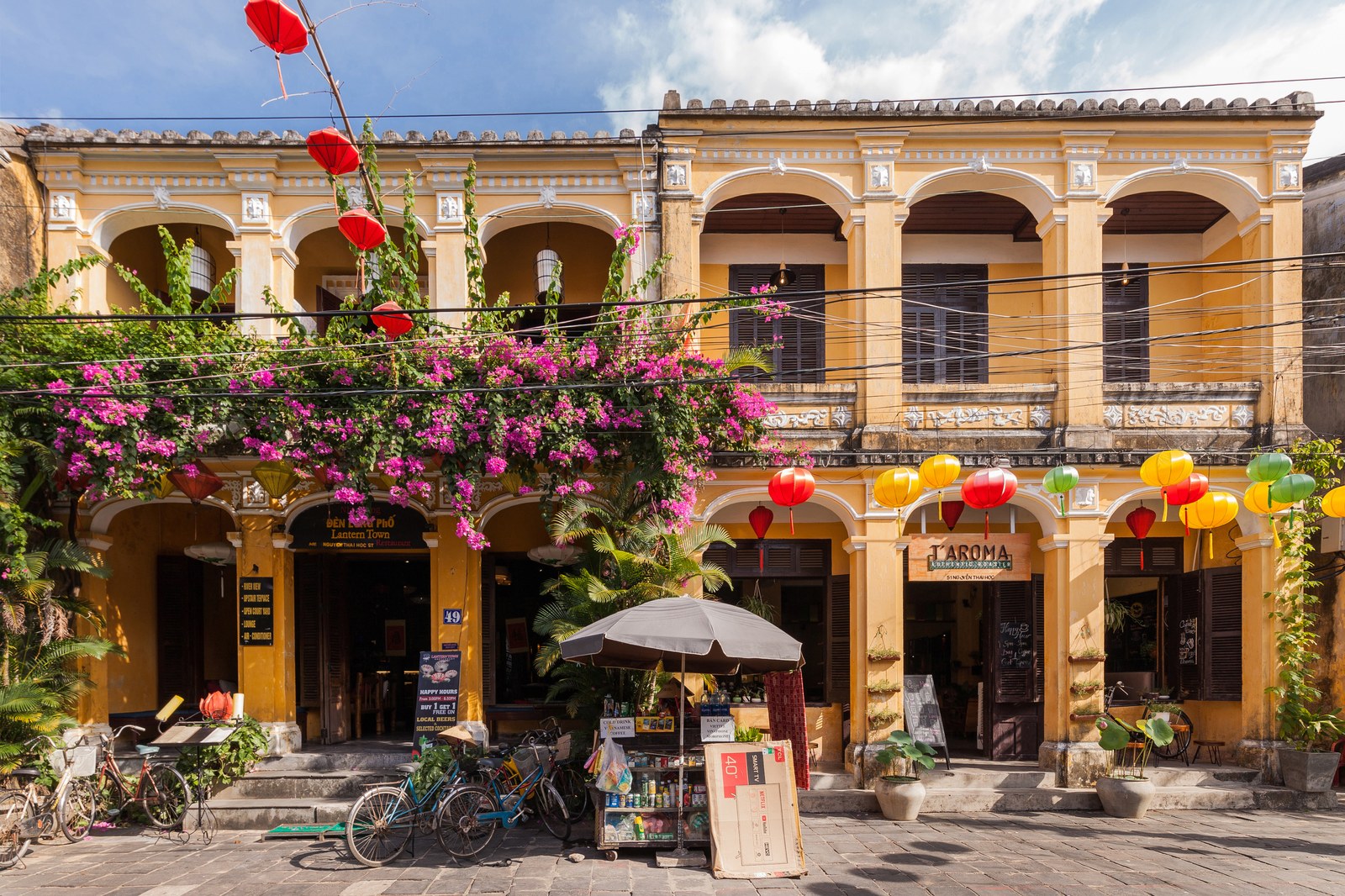 Dãy nhà cổ Hội An hai tầng nhìn từ dưới phố, một đèn lồng đỏ trắng và một đèn lồng hoa văn treo trên dây điện ngang qua đường