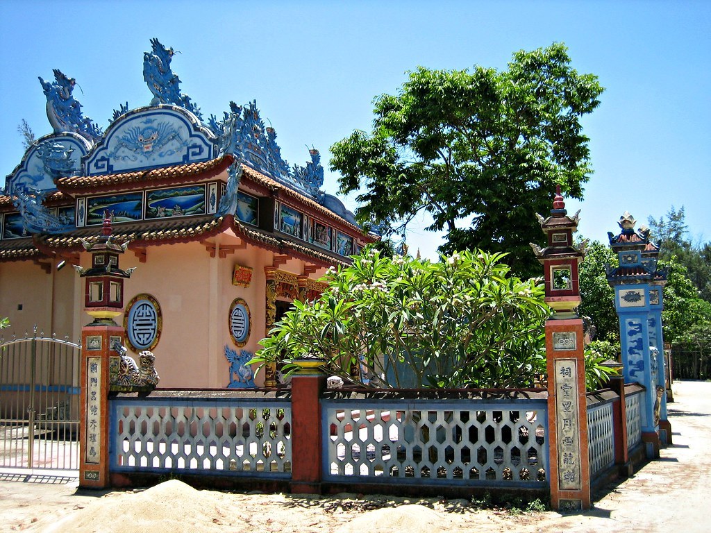 Cổng một nhà thờ họ ở Huế với hai trụ đá có tượng lân trên đỉnh, tường rào đắp nổi hình rồng màu xanh đỏ, cây xanh phía sau
