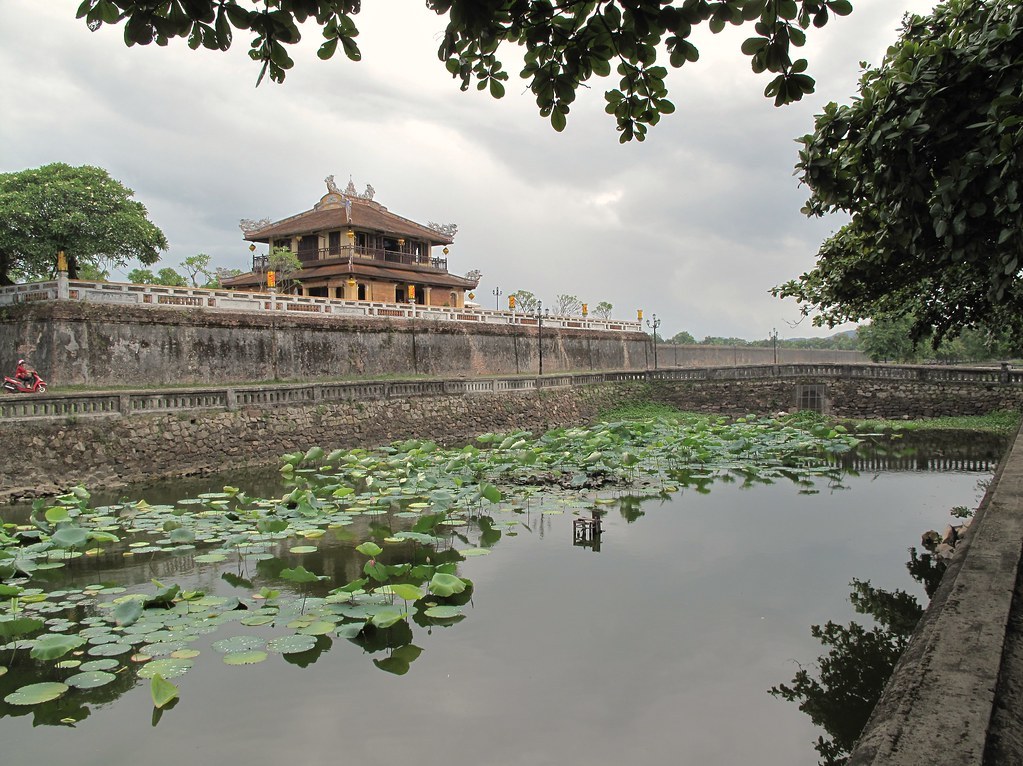 Một cổng thành trong Hoàng thành Huế nhìn từ xa qua mặt hồ có lá sen, tường thành bằng đá xây dọc theo bờ nước