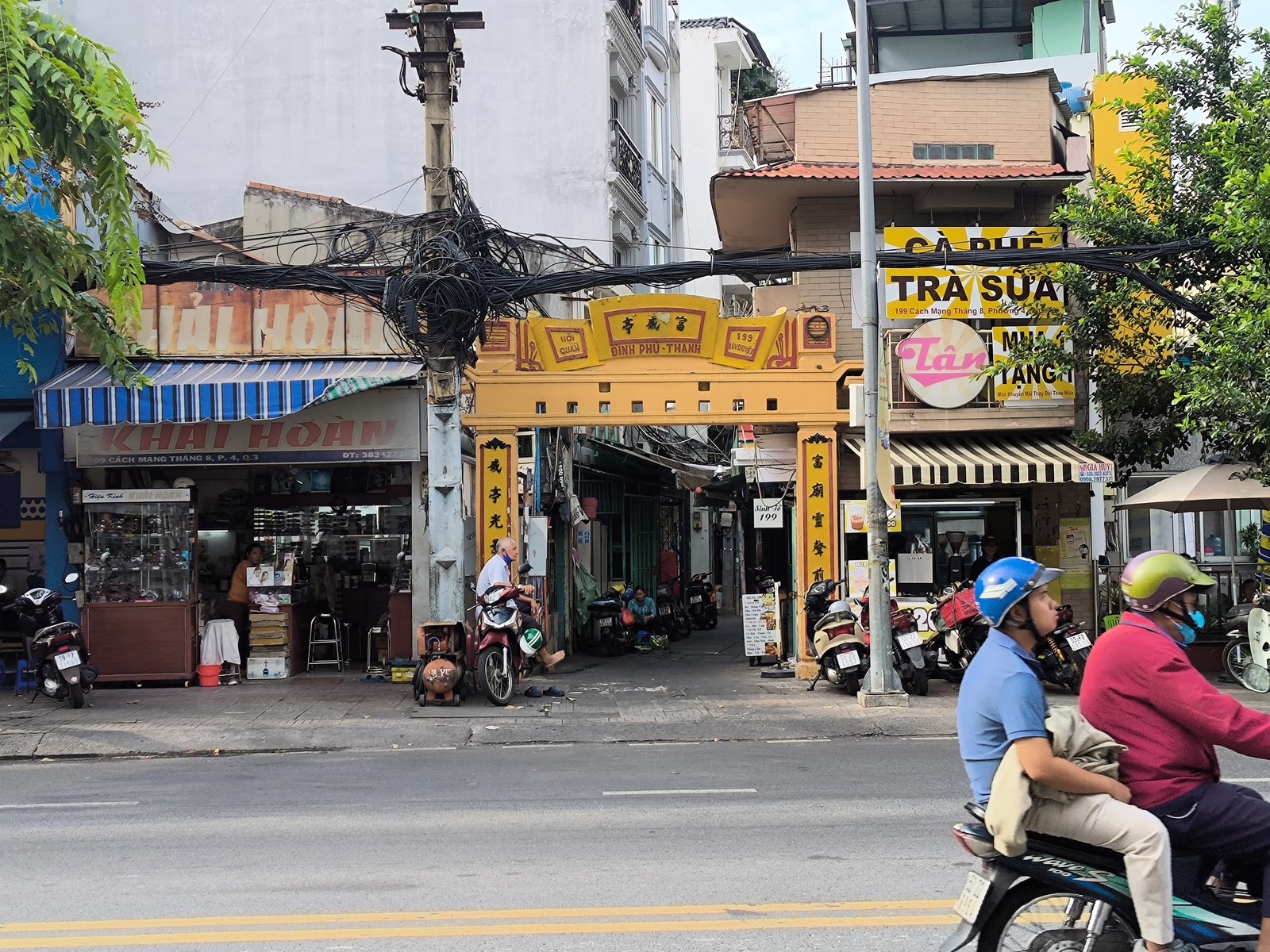Cổng tam quan màu vàng của Đình Phú Thạnh nằm lọt giữa hai dãy nhà phố với biển hiệu quán ăn, cà phê, dây điện chằng chịt phía trên