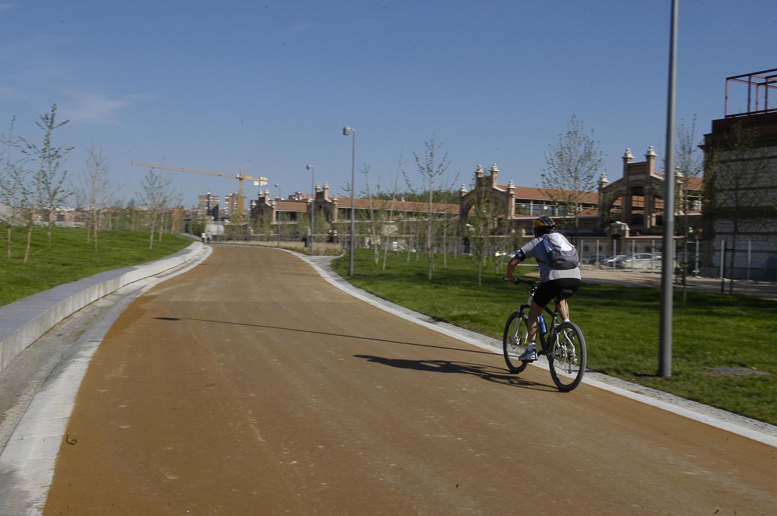 Người đạp xe trên làn đường riêng, phía sau là dãy nhà gạch cũ của khu Matadero Madrid