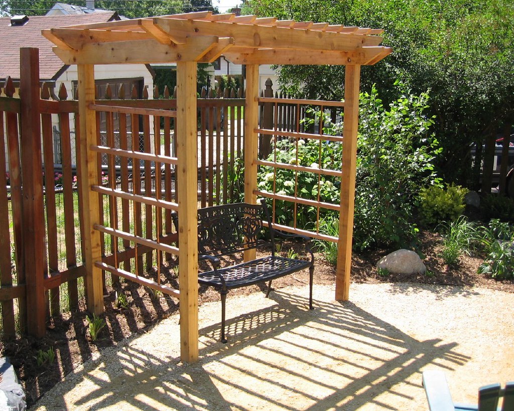 Giàn pergola gỗ trên sân sau, ghế sắt kê dưới bóng giàn, sát hàng rào gỗ có hoa leo