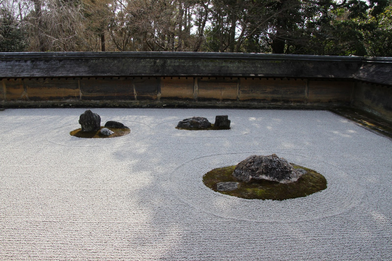 Vườn khô Ryōan-ji nhìn toàn cảnh: sân sỏi rải rộng, các cụm đá đặt rời nhau, tường đất thấp bao ba phía
