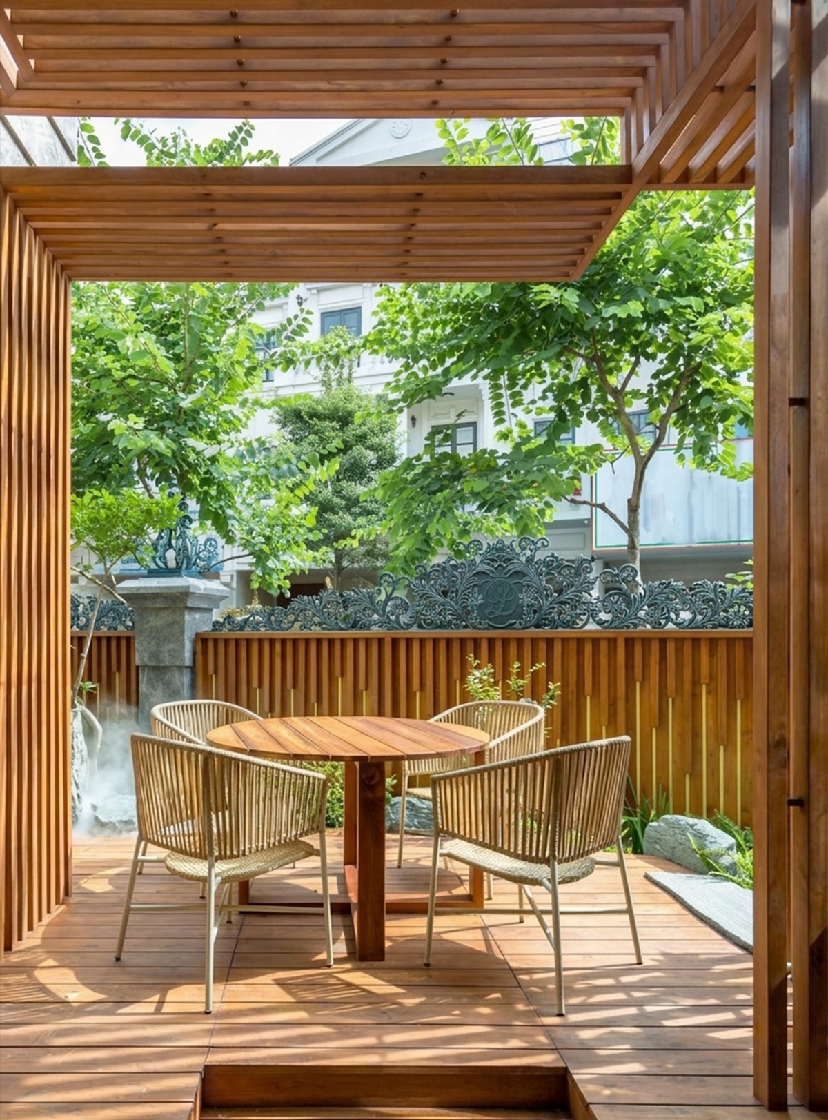 Chòi khung gỗ mái dốc che một sàn gỗ ngoài trời, bàn tròn và ghế mây đặt giữa, nhìn ra vườn qua vách lam gỗ